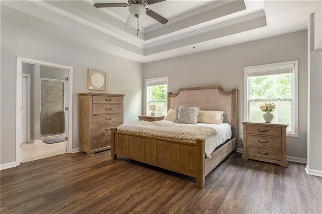 Bedroom featuring a raised ceiling, crown molding, dark wood finished floors, and ceiling fan
