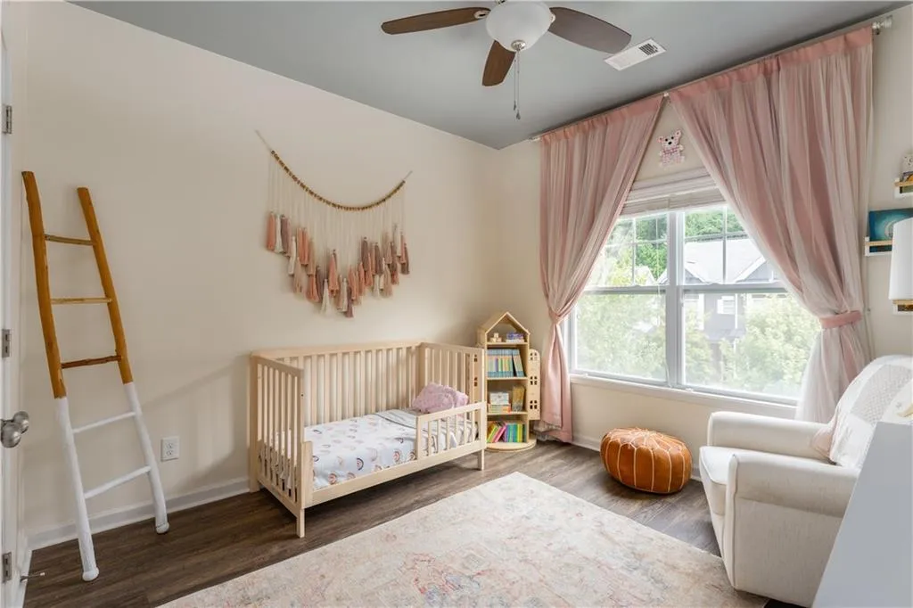 Bedroom featuring a nursery area, wood finished floors, and a ceiling fan