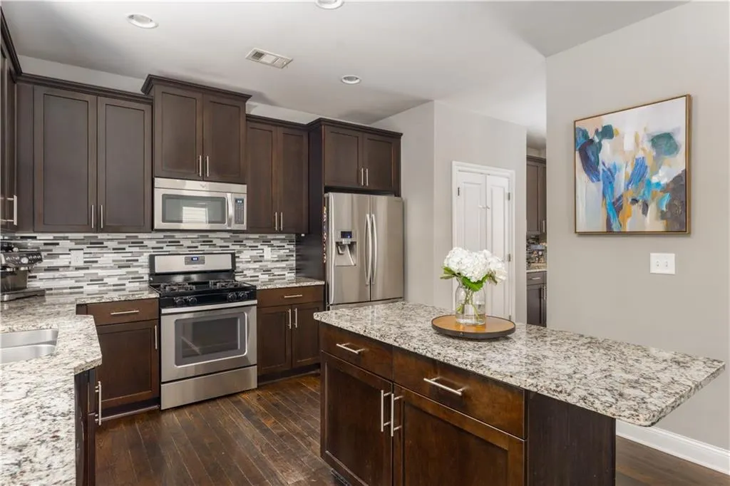 Kitchen featuring stainless steel appliances, dark wood finished floors, dark brown cabinetry, tasteful backsplash, and light stone countertops