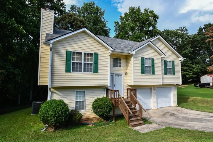 Split-level residence featuring light-colored siding, dark green window shutters, and a prominent front entrance with a wood-finish staircase