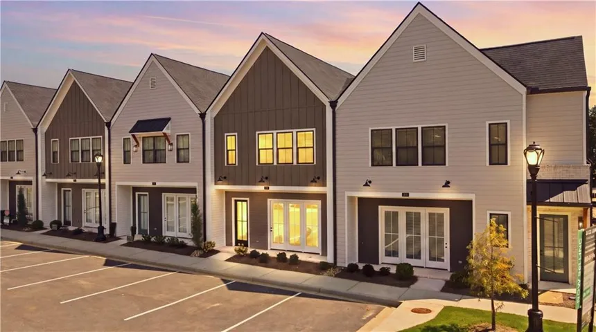 Contemporary townhome architecture featuring gabled roofs, a mix of light and dark siding, multiple windows, and a paved parking area