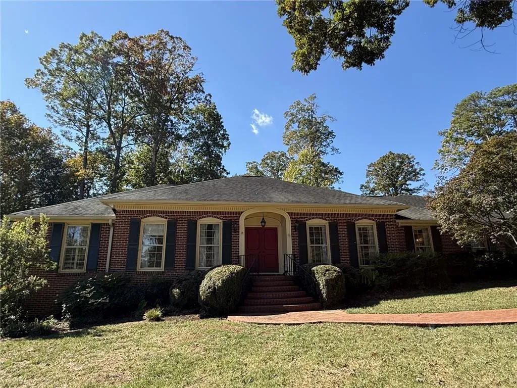 Single story home with a porch, a front lawn, brick siding, and a shingled roof