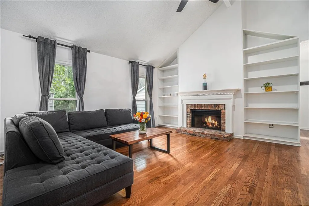 Living room with a textured ceiling, healthy amount of natural light, wood finished floors, a brick fireplace, and high vaulted ceiling Living room with a textured ceiling, healthy amount of natural light, wood finished floors, a brick fireplace, and high vaulted ceiling