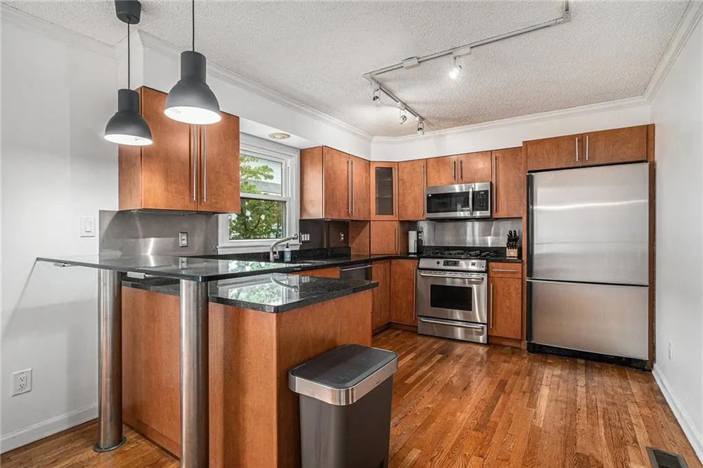 Kitchen featuring a textured ceiling, appliances with stainless steel finishes, pendant lighting, rail lighting, and brown cabinets Kitchen featuring a textured ceiling, appliances with stainless steel finishes, pendant lighting, rail lighting, and brown cabinets