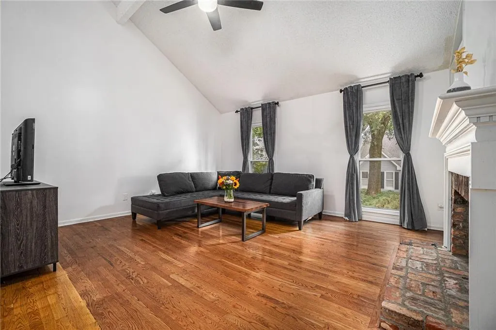 Living room with high vaulted ceiling, wood finished floors, a fireplace with raised hearth, and a textured ceiling Living room with high vaulted ceiling, wood finished floors, a fireplace with raised hearth, and a textured ceiling