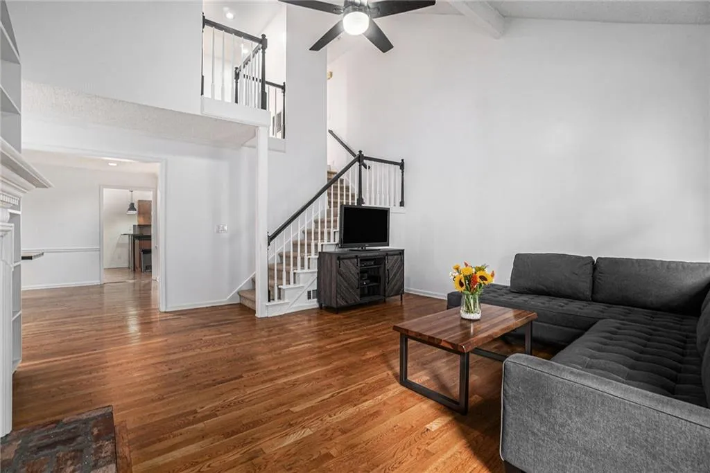 Living room featuring beam ceiling, wood finished floors, high vaulted ceiling, ceiling fan, and stairway Living room featuring beam ceiling, wood finished floors, high vaulted ceiling, ceiling fan, and stairway