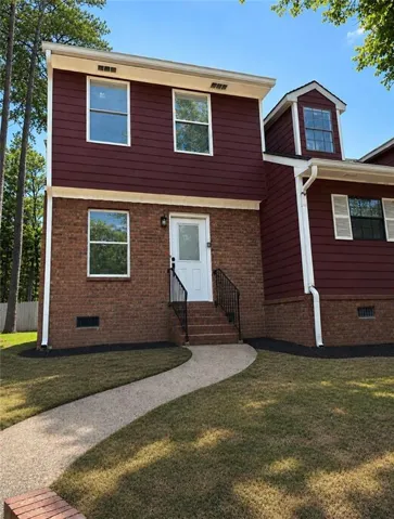 Exterior featuring brick and vertical siding, a front entry with white door and black handrails, a curved concrete walkway, and a dormer window