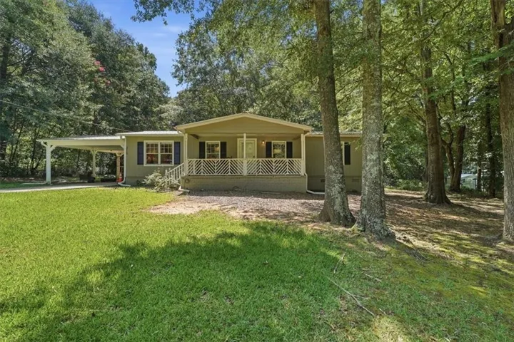 Expansive front lawn with mature trees, carport, covered front porch with railing, and exterior shutters