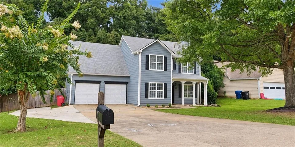 Two-story residence featuring siding, a front porch with columns, a two-car garage, and mature trees