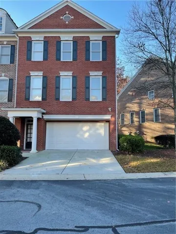 Brick exterior featuring a gabled roofline, multiple windows with dark shutters, and a two-car garage