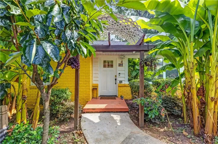 Entryway with a white paneled door, yellow brick exterior, and a wooden pergola featuring a white lattice accent