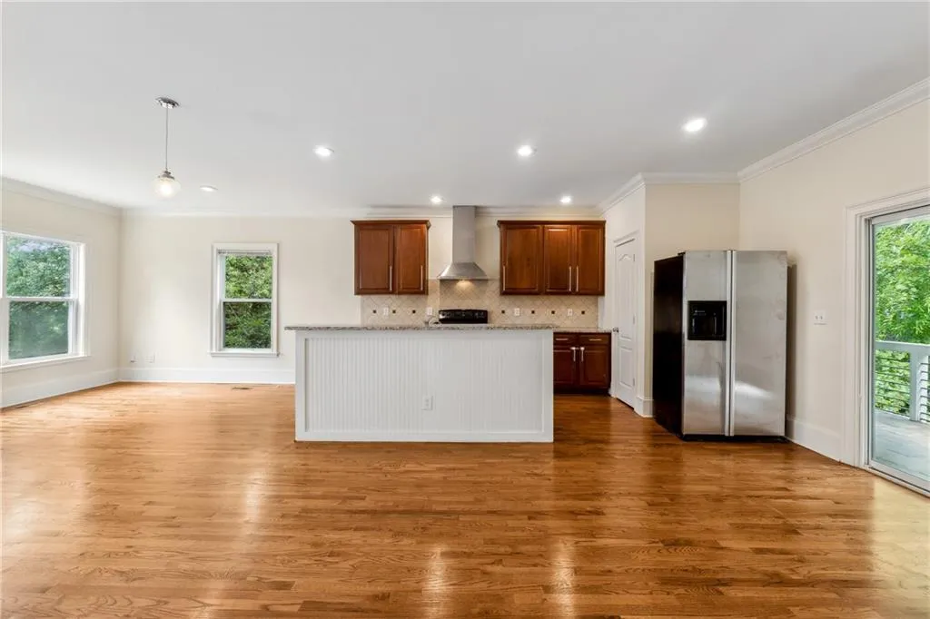 Kitchen with wall chimney range hood, hanging light fixtures, wood-type flooring, stainless steel refrigerator with ice dispenser, and ornamental molding