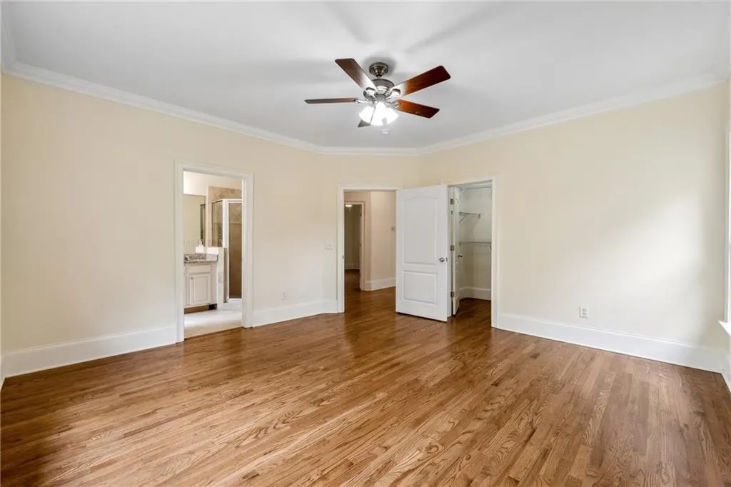 Unfurnished bedroom featuring a spacious closet, hardwood / wood-style flooring, ceiling fan, crown molding, and ensuite bathroom