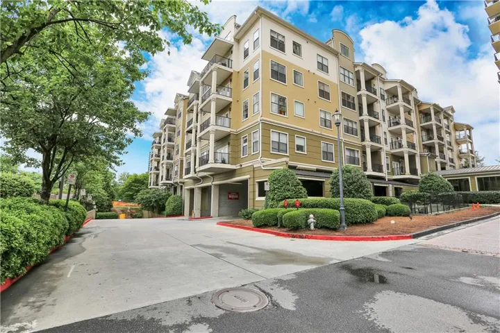 Multi-story residential building featuring a painted exterior, private balconies with black railings, and a ground-level parking area