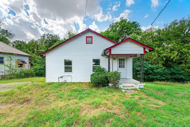 White siding exterior with a covered front porch featuring decorative metal supports, an attic window, and an entry door with a multi-pane window