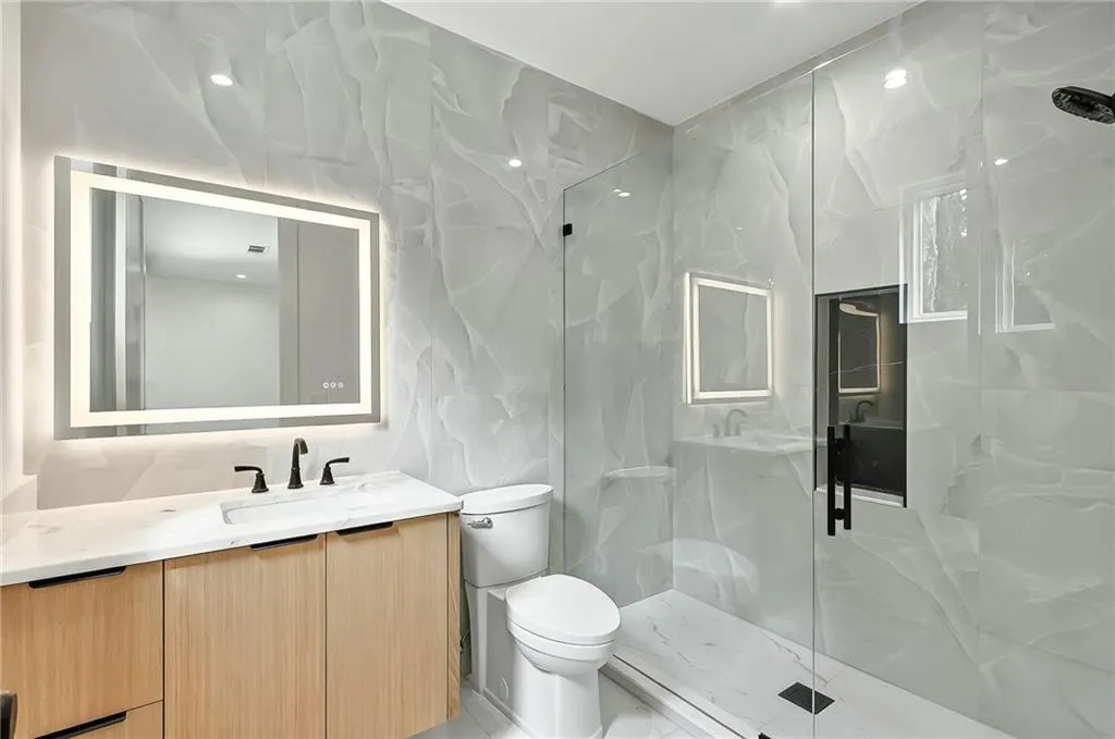 Bathroom with vanity, a marble finish shower, toilet, and tile walls