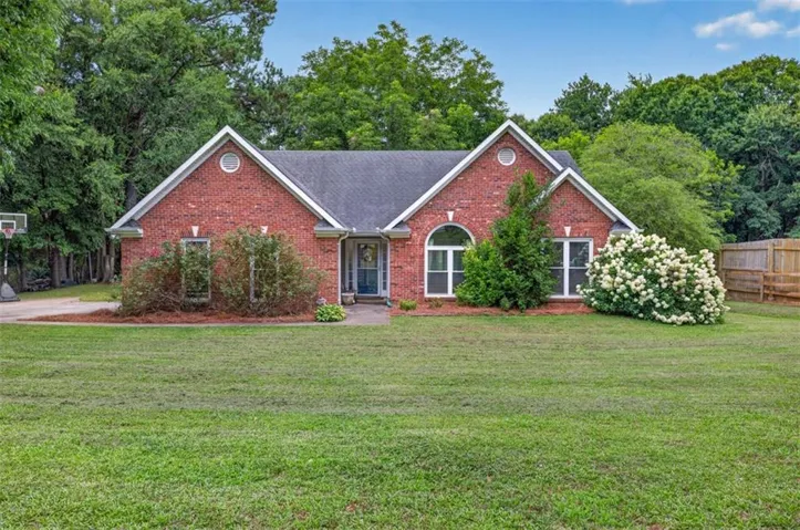 Brick exterior with gabled rooflines, a wide lawn, a paved driveway, and mature landscaping