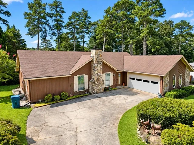 Brown siding exterior with a brown shingle roof, stone-clad chimney, and an attached two-car garage