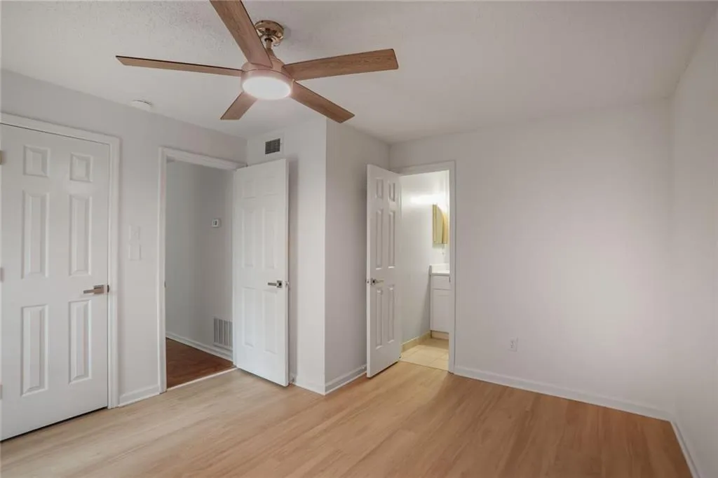 Unfurnished bedroom with light wood-style floors, baseboards, connected bathroom, and a ceiling fan