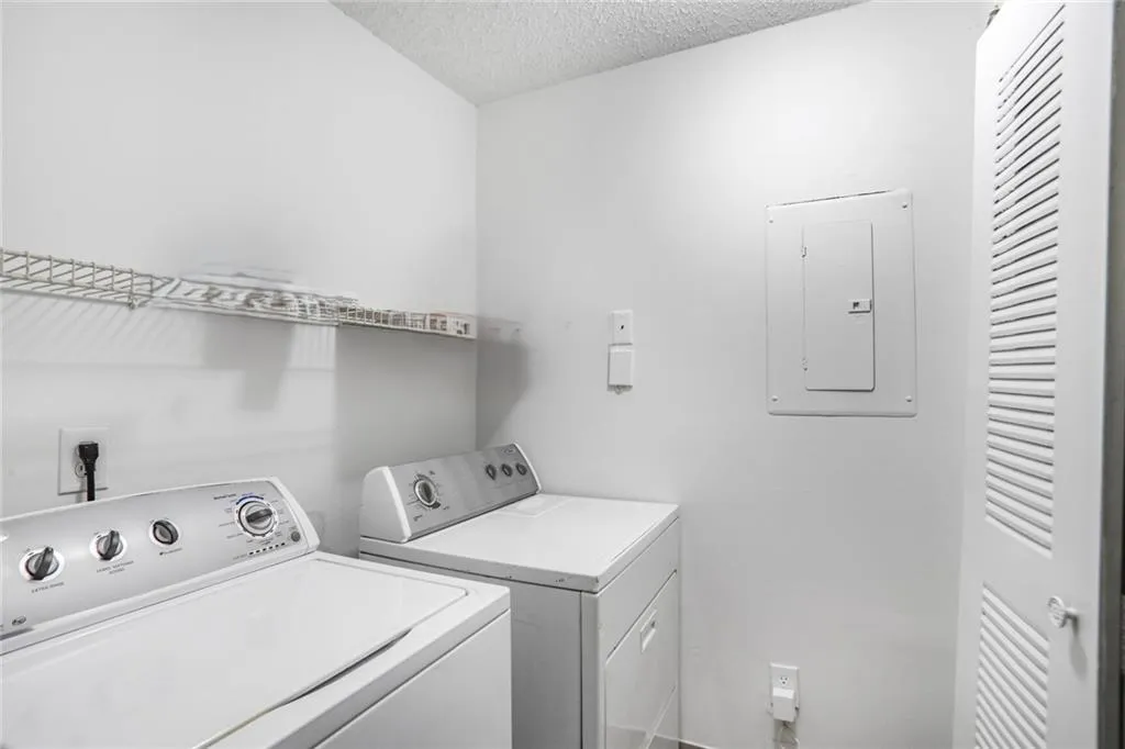 Laundry area with electric panel, separate washer and dryer, and a textured ceiling