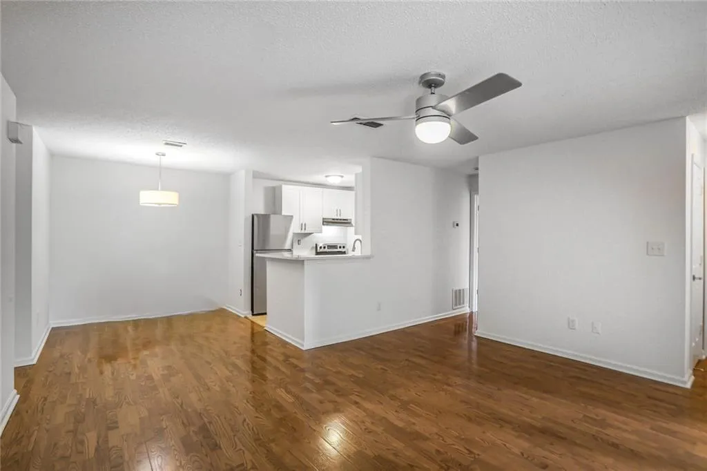 Unfurnished living room featuring dark wood-style flooring, ceiling fan, a textured ceiling, and baseboards