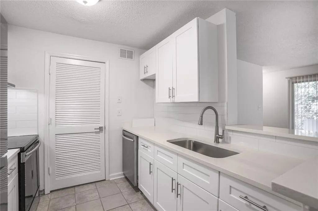 Kitchen featuring a sink, appliances with stainless steel finishes, a textured ceiling, white cabinetry, and light countertops