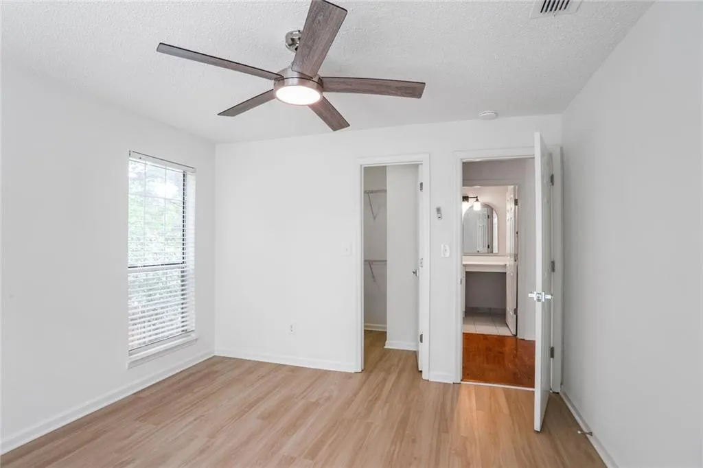 Unfurnished bedroom featuring light wood-style flooring, a walk in closet, a textured ceiling, a closet, and a ceiling fan