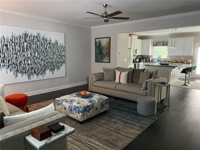 Open-concept living area featuring wood-finish flooring, a ceiling fan, and crown molding