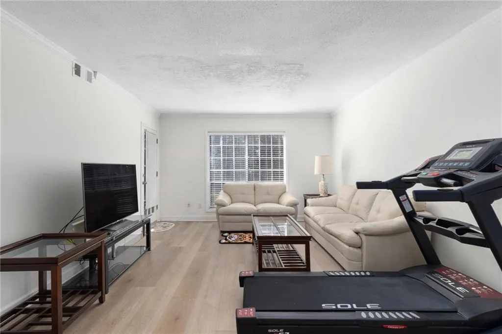 Living area with crown molding, light wood finished floors, and a textured ceiling