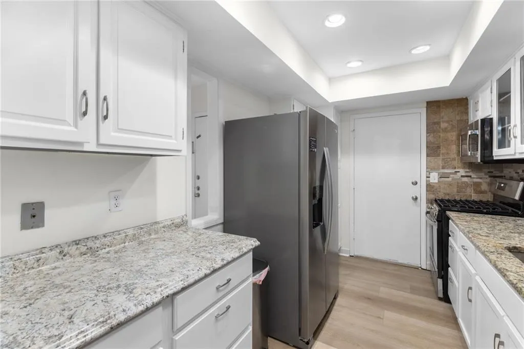 Kitchen featuring stainless steel appliances, glass insert cabinets, white cabinets, light wood-style flooring, and recessed lighting