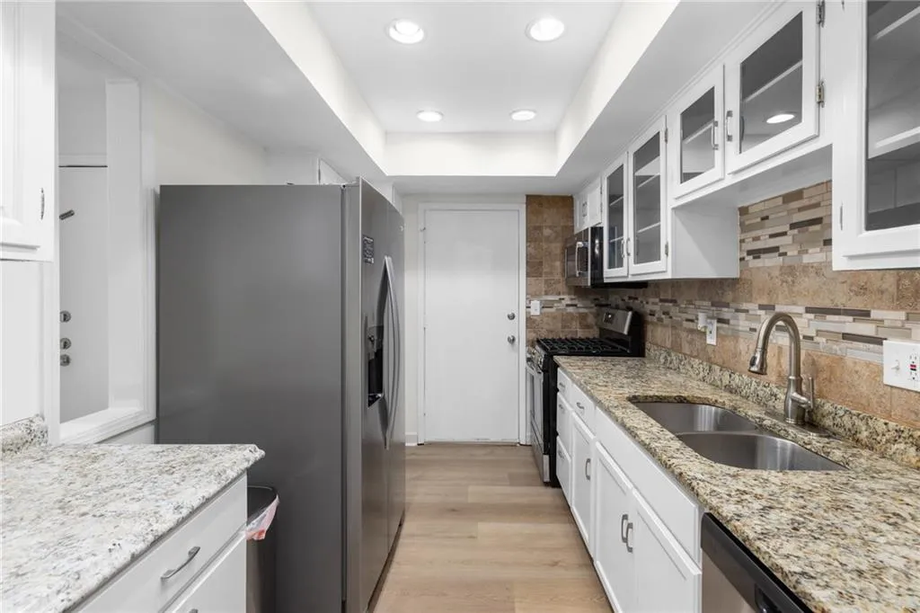 Kitchen featuring white cabinetry, appliances with stainless steel finishes, glass insert cabinets, light wood-style flooring, and recessed lighting
