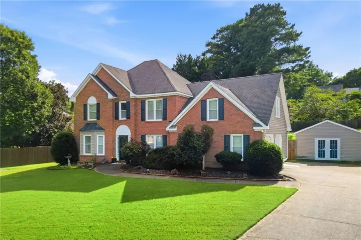 Brick and siding exterior featuring a multi-gable roofline, attached two-car garage, and a separate detached shed with double doors
