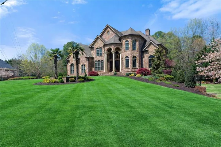 Stately brick exterior featuring multiple arched windows, prominent white columns, a meticulously manicured lawn, established landscaping, and mature palm trees