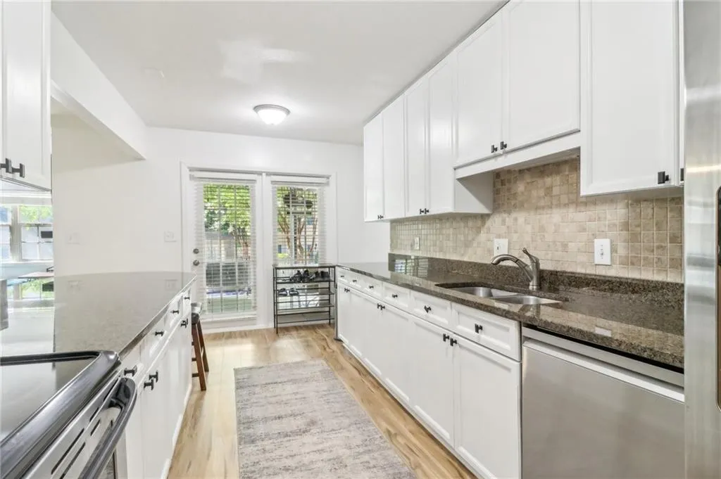 Kitchen with appliances with stainless steel finishes, dark stone counters, sink, light wood-type flooring, and white cabinetry Kitchen with appliances with stainless steel finishes, dark stone counters, sink, light wood-type flooring, and white cabinetry