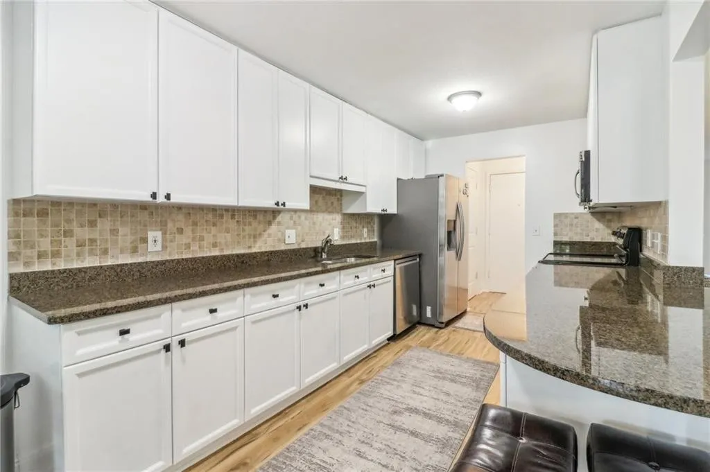 Kitchen with appliances with stainless steel finishes, dark stone countertops, decorative backsplash, and light wood-type flooring Kitchen with appliances with stainless steel finishes, dark stone countertops, decorative backsplash, and light wood-type flooring