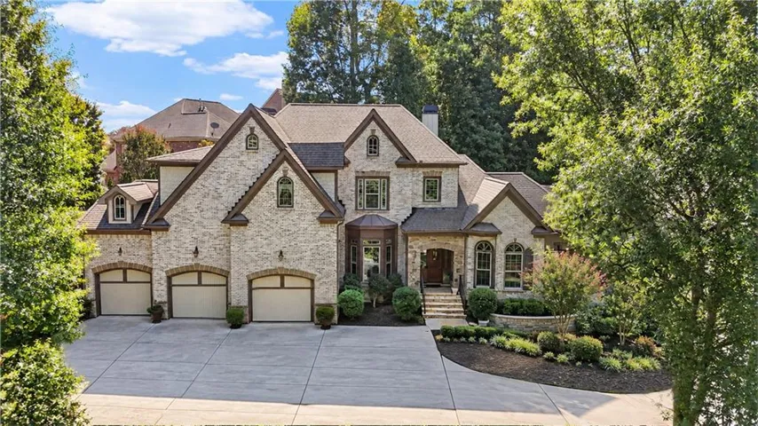 Stone facade residence featuring a multi-car garage, expansive driveway, and architectural roof shingles