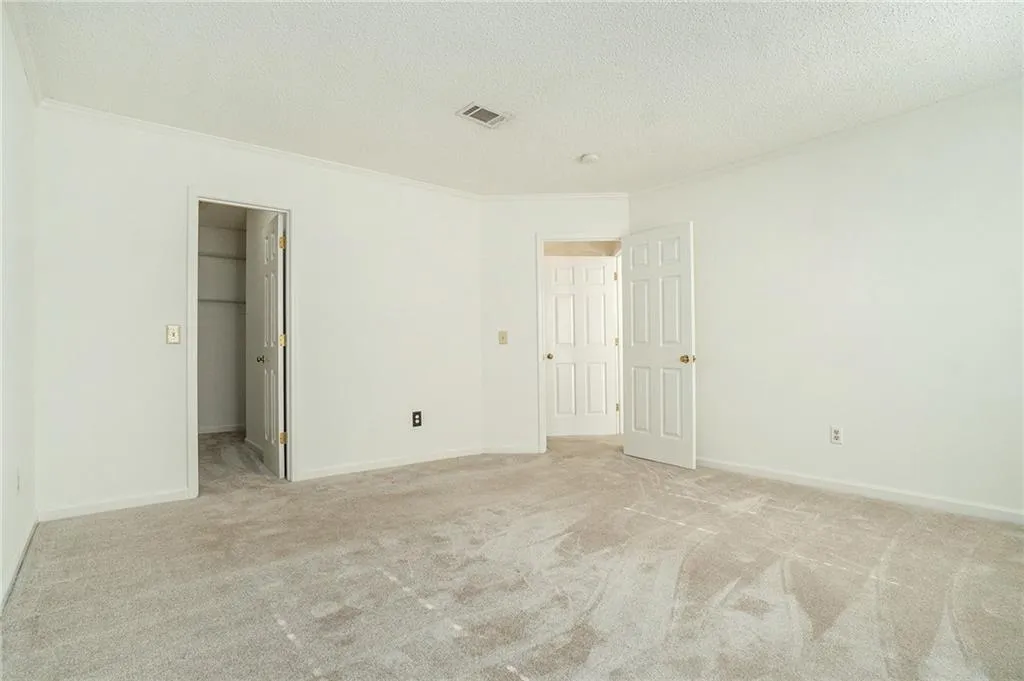 Unfurnished bedroom featuring a textured ceiling, a walk in closet, light carpet, and ornamental molding