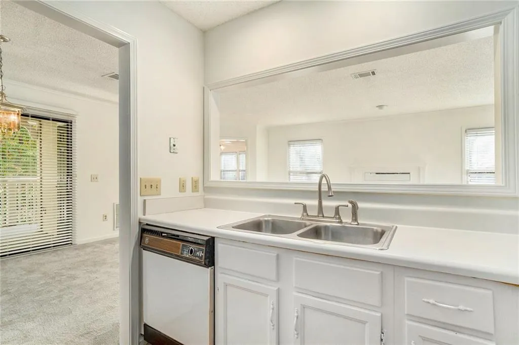 Kitchen featuring light carpet, white dishwasher, sink, a textured ceiling, and white cabinetry