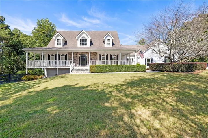 Traditional-style residence featuring a wide wrap-around porch, stone accents, multiple dormer windows, and a manicured lawn
