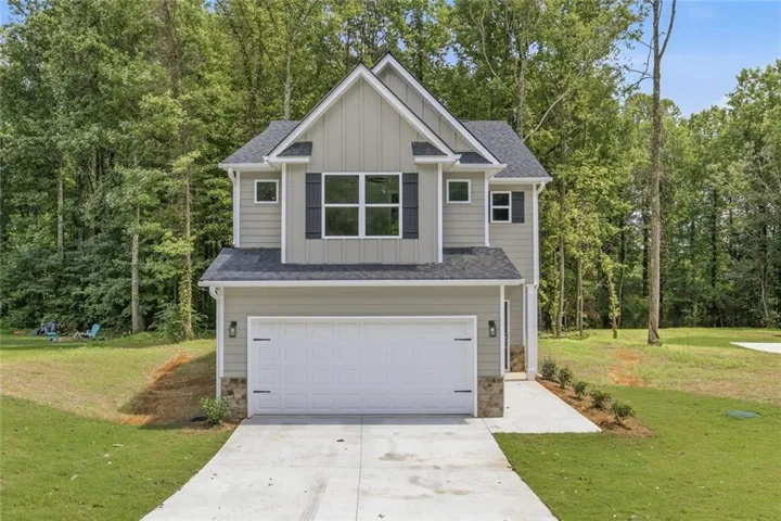 Two-story residence featuring light gray siding, dark shutters, an attached two-car garage, and a concrete driveway