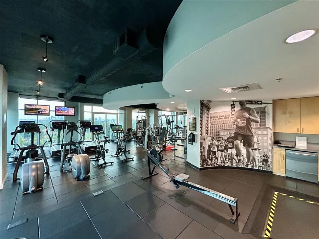 Fitness center featuring extensive exercise equipment, dark tile flooring, exposed ductwork, and abundant natural light from large windows