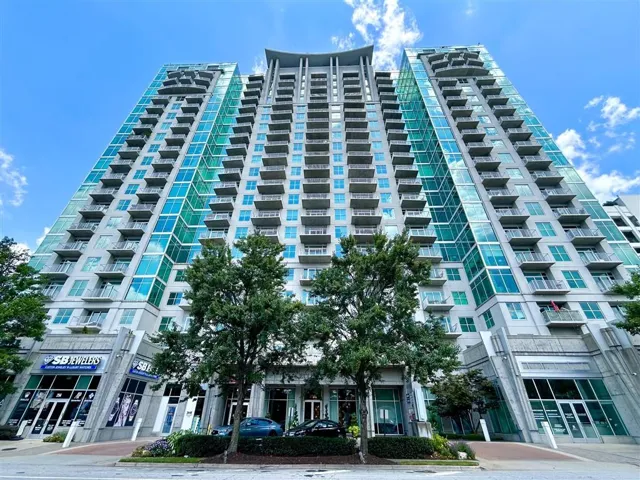 Contemporary high-rise architecture featuring a prominent glass facade, individual balconies, and ground-level retail spaces