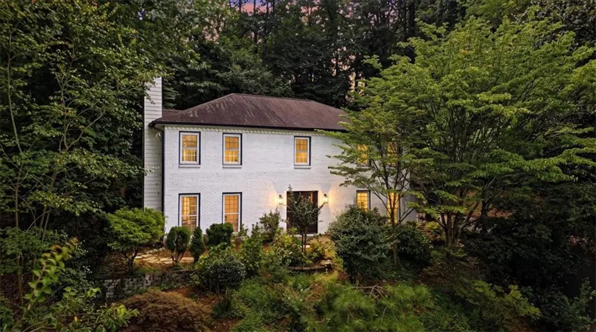 White brick two-story residence featuring a dark roof and a prominent chimney