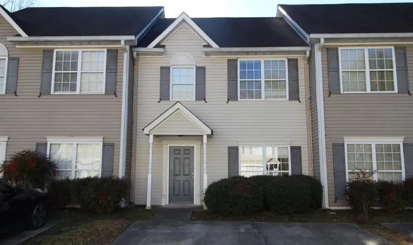 Two-story exterior with light-toned siding, dark roof, prominent window shutters, and a covered entryway