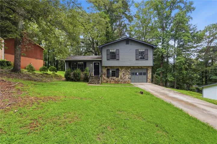 Split-level residence featuring a stone and siding exterior, an attached garage, a covered entry porch, and a screened-in porch