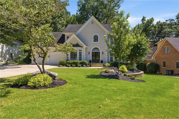 Front exterior featuring a light-colored stucco finish, multi-pane windows, a prominent arched entryway, and a two-car garage