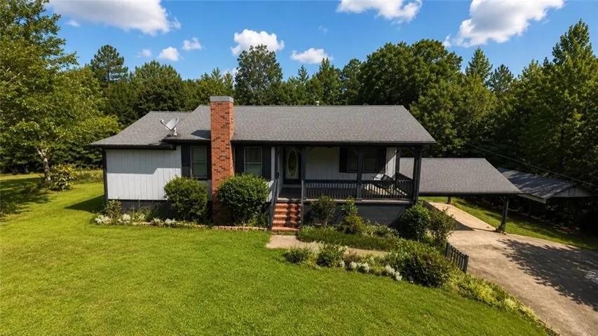 Ranch-style residence featuring a prominent brick chimney and a covered front porch with dark railings