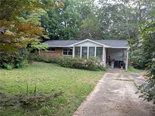 Brick exterior with a covered carport, enclosed porch, and mature surrounding trees