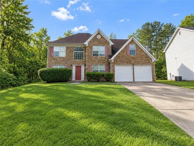 Stone veneer facade, two-car garage, red front door, arched window, and established landscaping