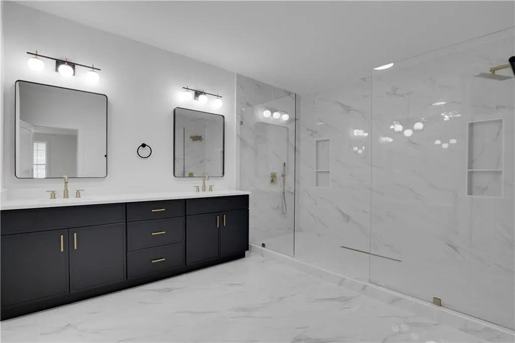 Bathroom with light marble finish flooring, a marble finish shower, and double vanity